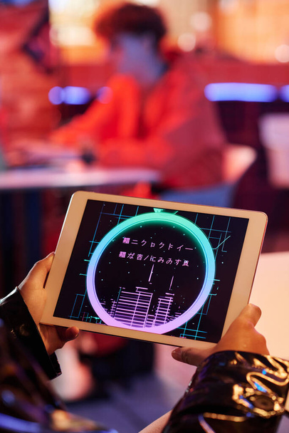 Group of hieroglyphs without meaning on screen of tablet held by cyberpunk girl spending free time in cyberpunk bar or cafe - Photo, Image