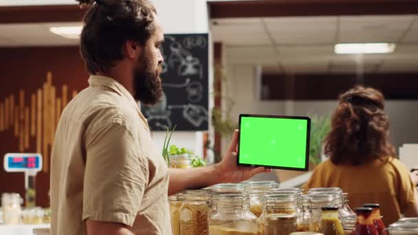 Kunde verwendet isolierte Bildschirmtabletten im Supermarkt, um Zutaten auf gesunde Rezepte zu überprüfen. Kunde in lokalem Lebensmittelgeschäft verwendet Attrappe Gerät beim Einkauf für Speisekammer Heftklammern - Filmmaterial, Video