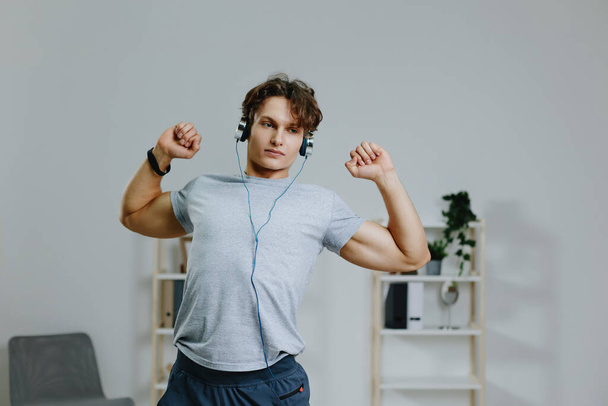 男性 物理的な屋内ボディスポーツ運動ヘッドフォン スポーツウェア 灰色活動 ホームスポーティトレーニング アクティブなイヤホン チュートリアル 筋肉 健康的なライフスタイル運動 - 写真・画像