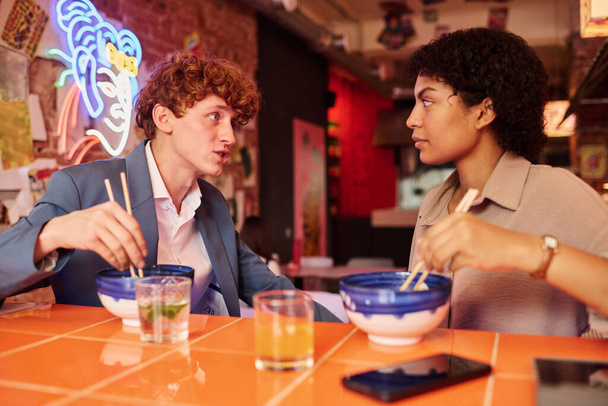 Zwei junge interkulturelle Kollegen oder Dates beim Plaudern in der Mittagspause im japanischen Café oder Restaurant, während sie Ramen essen und einander anschauen - Foto, Bild