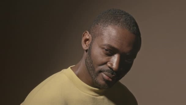 Mellkas fel portré jóképű afro-amerikai férfi emelte fel a szemét lassan a kamera és mosolygós álló sötét stúdió háttér - Felvétel, videó
