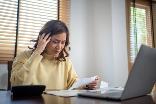 Een vrouw gebruikt een rekenmachine om de som van haar huiskosten te controleren en ze is gestrest over de huiskosten. - Foto, afbeelding