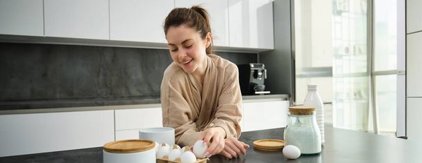 Приваблива молода весела дівчина випікає на кухні, робить тісто, тримає книгу рецептів, має ідеї
. - Фото, зображення