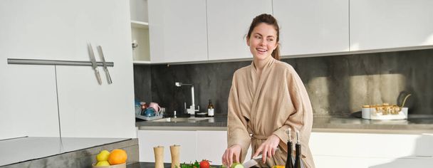 Портрет щасливої жінки, що рубає овочі на дошці, стоїть на кухні, готує їжу для себе, здорову їжу, готує смачний свіжий салат і посміхається. - Фото, зображення