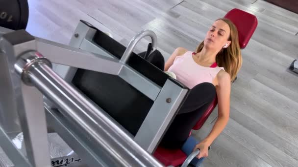 Mujer deportiva entrena los músculos de sus piernas en la máquina de ejercicios en el gimnasio. Imágenes de alta calidad 4k - Imágenes, Vídeo
