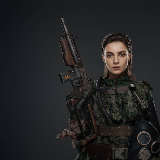 Retrato de uma soldado em traje militar, segurando uma espingarda automática caseira, retratando uma rebelde ou partidária em um conflito no Oriente Médio contra um fundo cinza - Foto, Imagem