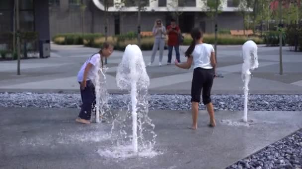 Kuumana päivänä lapset juoksevat ja pitävät hauskaa kaupungin suihkulähteellä. Vapaa-ajan käsite. kesälomat. Onnellinen lapsu Laadukas kuva - Materiaali, video