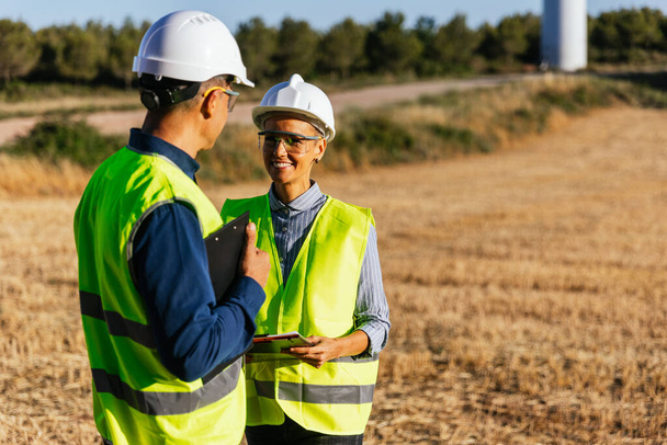Optimistic engineers working on a windmill farm, standing in the field on a sunny day. - Photo, Image