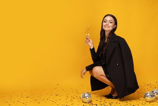Chica con champán y copas sobre un fondo amarillo. - Foto, Imagen
