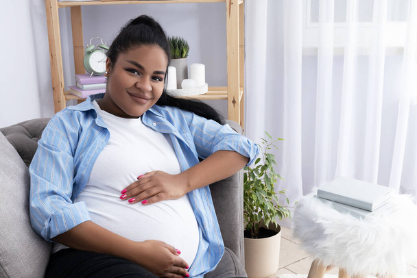 Mujer afroamericana embarazada en la habitación en el sofá. - Foto, imagen