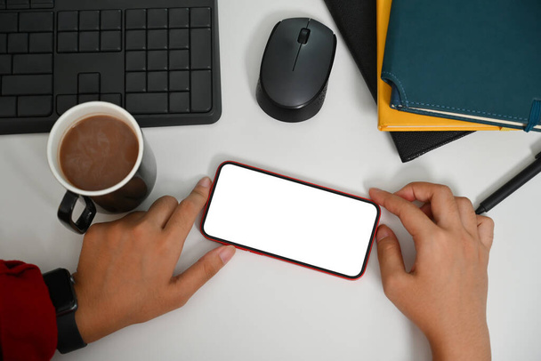 白いオフィスの机で携帯電話を使用する女性の眺めの上. テキストメッセージを広告するための空のスクリーン. - 写真・画像