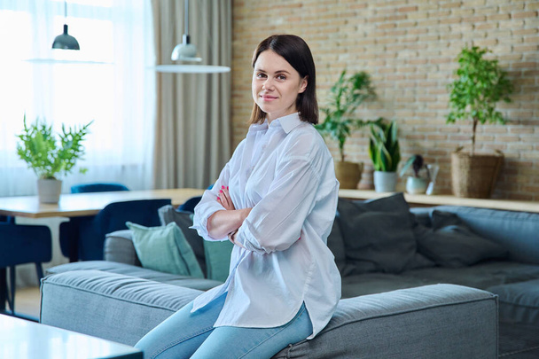Portrait of confident smiling successful young woman 30 years old with crossed arms looking at the camera in the living room. Beauty, confidence, success, lifestyle, people concept - Foto, imagen