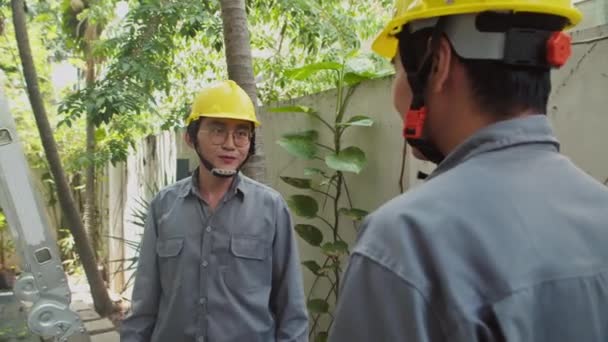 Mediana toma de reparador en sombrero duro dando caja de herramientas a su compañero de trabajo que se prepara para trabajar en el techo - Metraje, vídeo