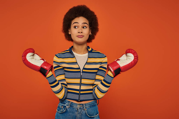 confused sporty african american woman posing actively with boxing gloves on orange backdrop - Fotografie, Obrázek