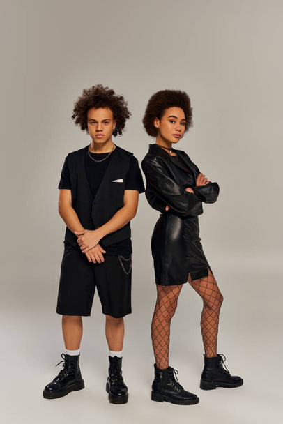 atraktivní trendy afroameričtí sourozenci v módních černých kostýmech pózují aktivně spolu - Fotografie, Obrázek