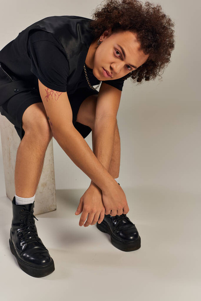 giovane modello afroamericano maschio in nero urbano elegante abbigliamento posa attivamente su sfondo grigio - Foto, immagini