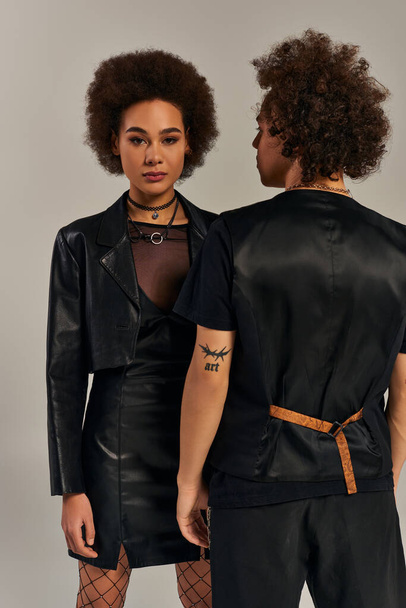 módní afroameričtí sourozenci ve stylovém černém městském oblečení pózující společně na šedém pozadí - Fotografie, Obrázek