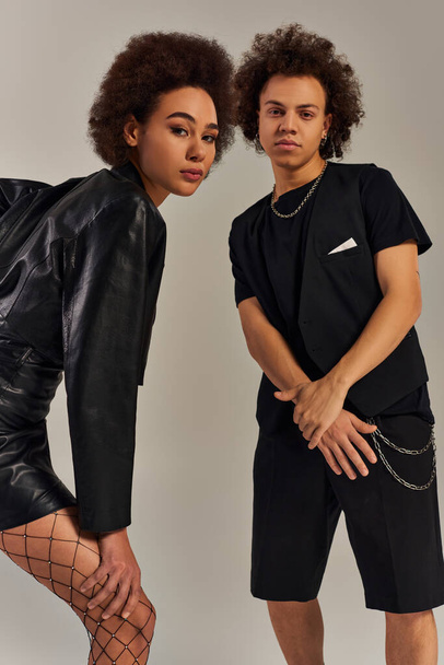 atraktivní afroameričtí sourozenci ve stylovém černém městském oblečení pózující společně na šedém pozadí - Fotografie, Obrázek