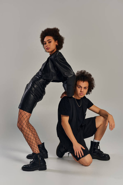 stylish african american brother and sister in black outfit posing on gray backdrop, fashion - Photo, Image