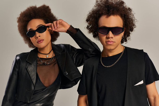 portret młodego afrykańskiego rodzeństwa w czarnych ubraniach z okularami przeciwsłonecznymi na szarym tle - Zdjęcie, obraz