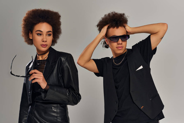 portrét mladých módních afrických amerických sourozenců v černých šatech se slunečními brýlemi na šedém pozadí - Fotografie, Obrázek