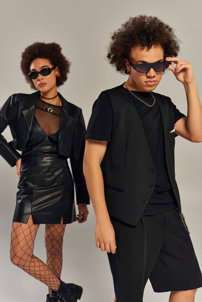 stylish african american brother and sister in trendy attire with sunglasses posing on gray backdrop - Photo, Image