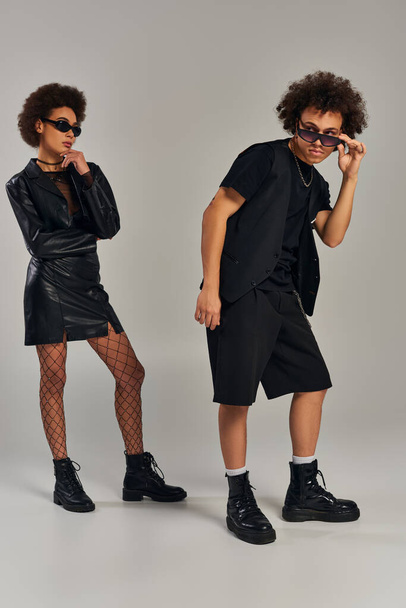 young african american siblings in trendy black attire with sunglasses posing on gray backdrop - Фото, изображение