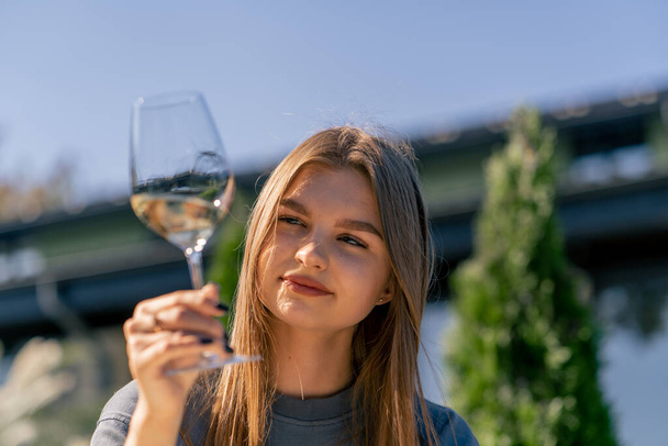 Close-up de uma menina bonita segurando um copo de vinho na mão, inalando seu aroma e degustando-o no terraço no jardim - Foto, Imagem