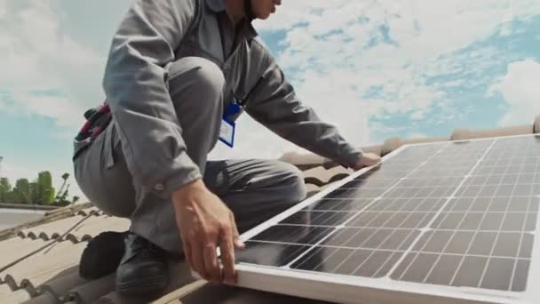 Mosolygó munkás portréja, amint napelemet telepít a tetőre és kamerába néz - Felvétel, videó