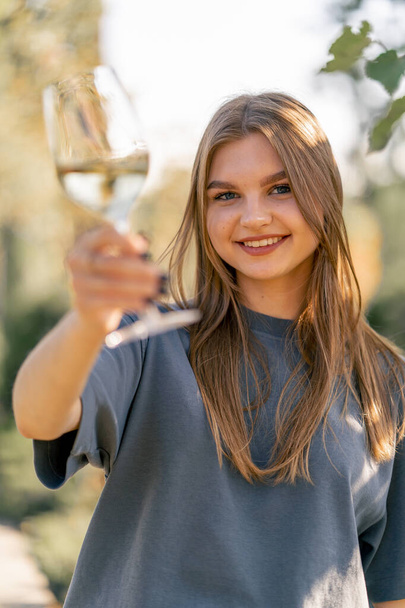 Retrato de uma linda menina de cabelos compridos toma um gole de vinho de um copo e entrega-o à câmera com um sorriso - Foto, Imagem