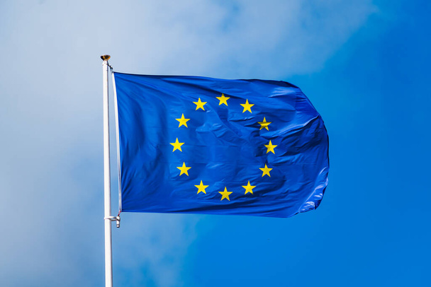 Bandera de Europa ondeando con viento fuerte y cielo azul, bandera azul con estrellas amarillas formando un círculo - Foto, Imagen