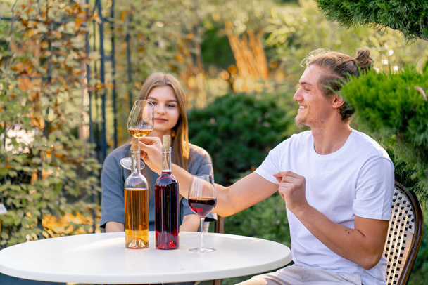 Una coppia di un ragazzo e una ragazza sono seduti insieme a un tavolo nel giardino di una cantina e degustazione di diversi tipi di vino - Foto, immagini
