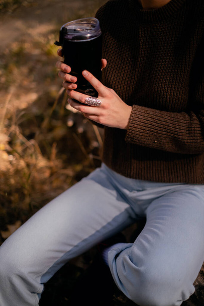 junge Frau entspannt sich an einem Herbsttag im Freien, reist in den Wald, sitzt auf einem Holzstamm im Wald und trinkt heißen Tee, Einheit mit der Natur, sucht nach dem Sinn des Lebens - Foto, Bild