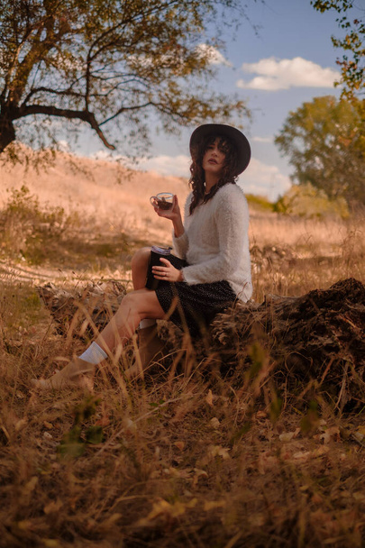 mujer joven relajándose al aire libre en un día de otoño, viajando al bosque, sentada en un tronco de madera en el bosque y bebiendo té caliente, unidad con la naturaleza, buscando el significado de la vida - Foto, imagen
