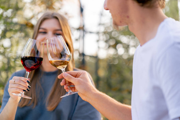 Κοντινό πλάνο ενός κοριτσιού που κλείνει ποτήρια με διαφορετικούς τύπους κρασιού με έναν άντρα να κάθεται μαζί στη βεράντα. - Φωτογραφία, εικόνα