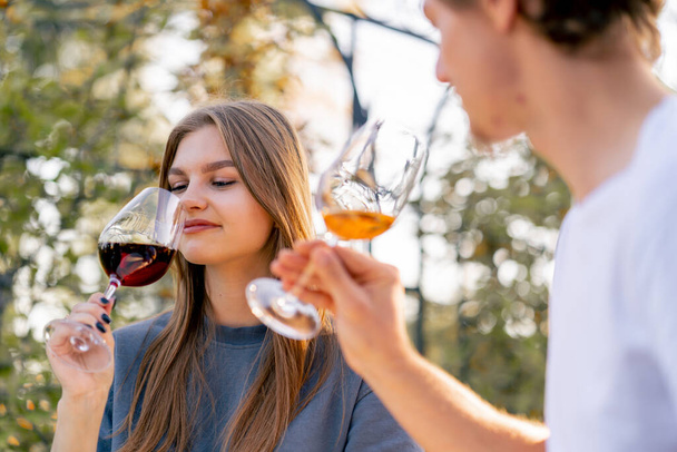 Κοντινό πλάνο ενός κοριτσιού που κλείνει ποτήρια με διαφορετικούς τύπους κρασιού με έναν άντρα να κάθεται μαζί στη βεράντα. - Φωτογραφία, εικόνα