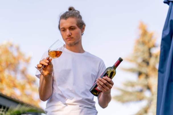 Αρσενικό επαγγελματικό sommelier ετοιμάζει ένα μπουκάλι κρασί για δοκιμή στους επισκέπτες στον κήπο του οινοποιείου - Φωτογραφία, εικόνα