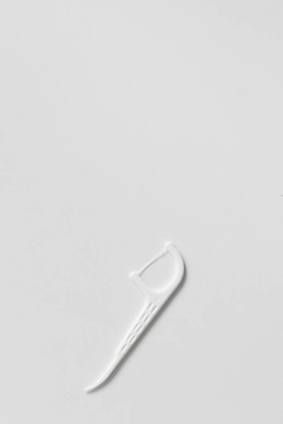 Πλαστική λευκή οδοντογλυφίδα με οδοντικό νήμα σε λευκό φόντο με copyspace - Φωτογραφία, εικόνα