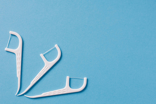 Τρεις πλαστικές λευκές οδοντογλυφίδες με οδοντικό νήμα σε μπλε φόντο - Φωτογραφία, εικόνα