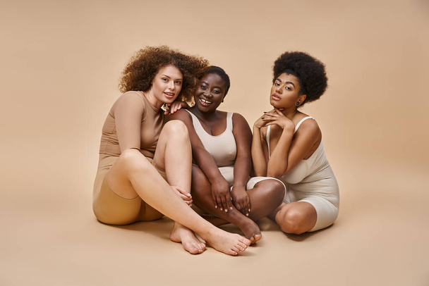 longueur totale de multiculturel plus la taille des copines en sous-vêtements assis sur beige, expression de soi - Photo, image