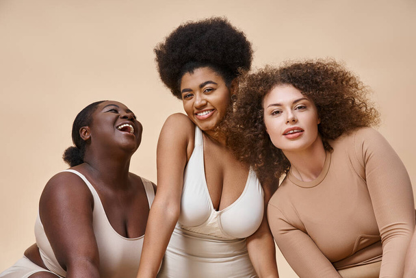 vreugdevolle multiraciale plus size vrouwen in ondergoed positief op beige, natuurlijk lichaam positieve schoonheid - Foto, afbeelding