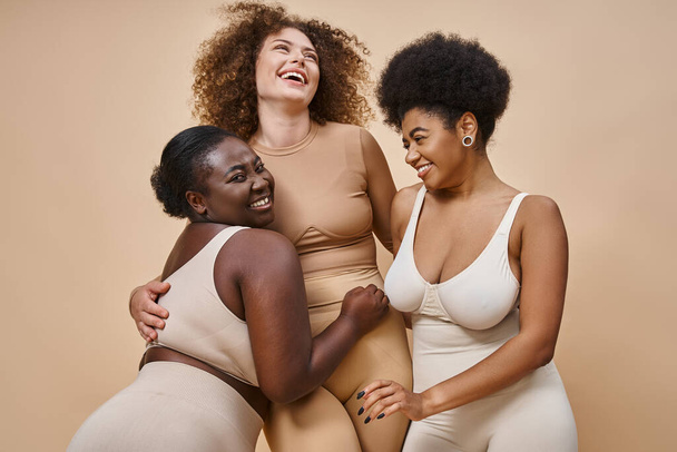 Bej arka plan, güzellik ve vücut pozitifliği üzerine poz veren iç çamaşırlı neşeli çok ırklı kadınlar. - Fotoğraf, Görsel