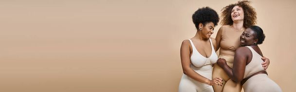 ベージュの背景,美しさと体のポジティブさ,バナーにポーズする下着の陽気な多人種の女性 - 写真・画像