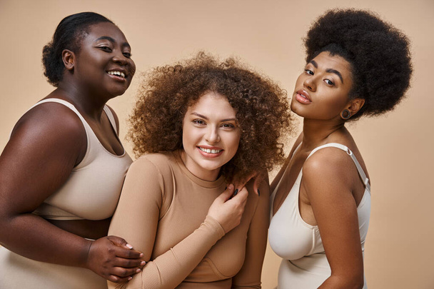 vidám multietnikus plusz méret barátnők fehérnemű pózol bézs háttér, test pozitivitás - Fotó, kép