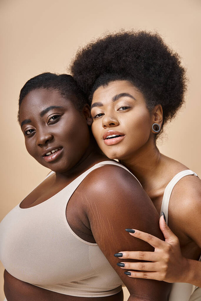 joyeux plus la taille des femmes afro-américaines en sous-vêtements en regardant la caméra sur beige, la positivité du corps - Photo, image