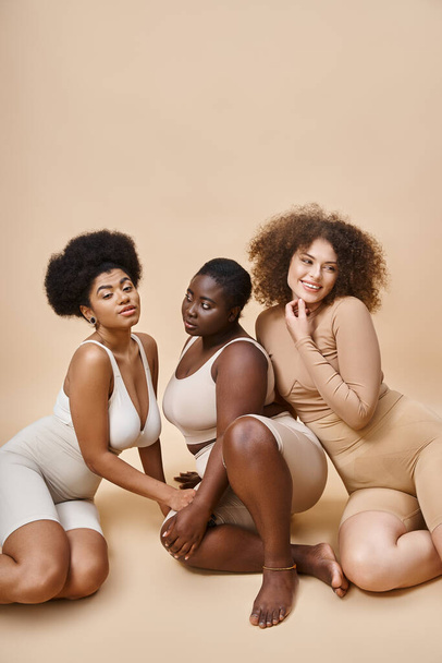happy multiracial body positive women in lingerie posing on beige backdrop, natural beauty - Photo, Image