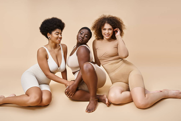okouzlující multiraciální ženy ve spodním prádle pózovat na béžové pozadí, plus velikost elegance a krásy - Fotografie, Obrázek