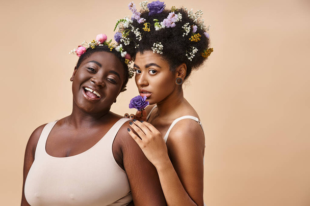 ベージュの下着に髪の毛の花を持つアフリカ系アメリカ人女性の笑顔,そしてサイズの美しさ - 写真・画像