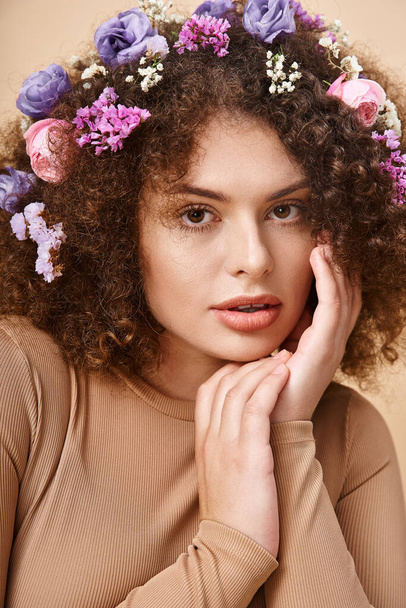 portrait of charming woman with flowers in wavy hair looking at camera on beige, natural beauty - Photo, Image