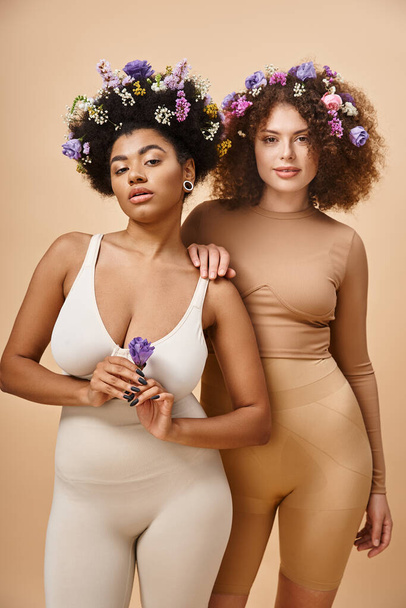 πολυφυλετικό σώμα θετικές γυναίκες σε εσώρουχα με πολύχρωμα λουλούδια στα μαλλιά σε μπεζ, συν το μέγεθος ομορφιά - Φωτογραφία, εικόνα